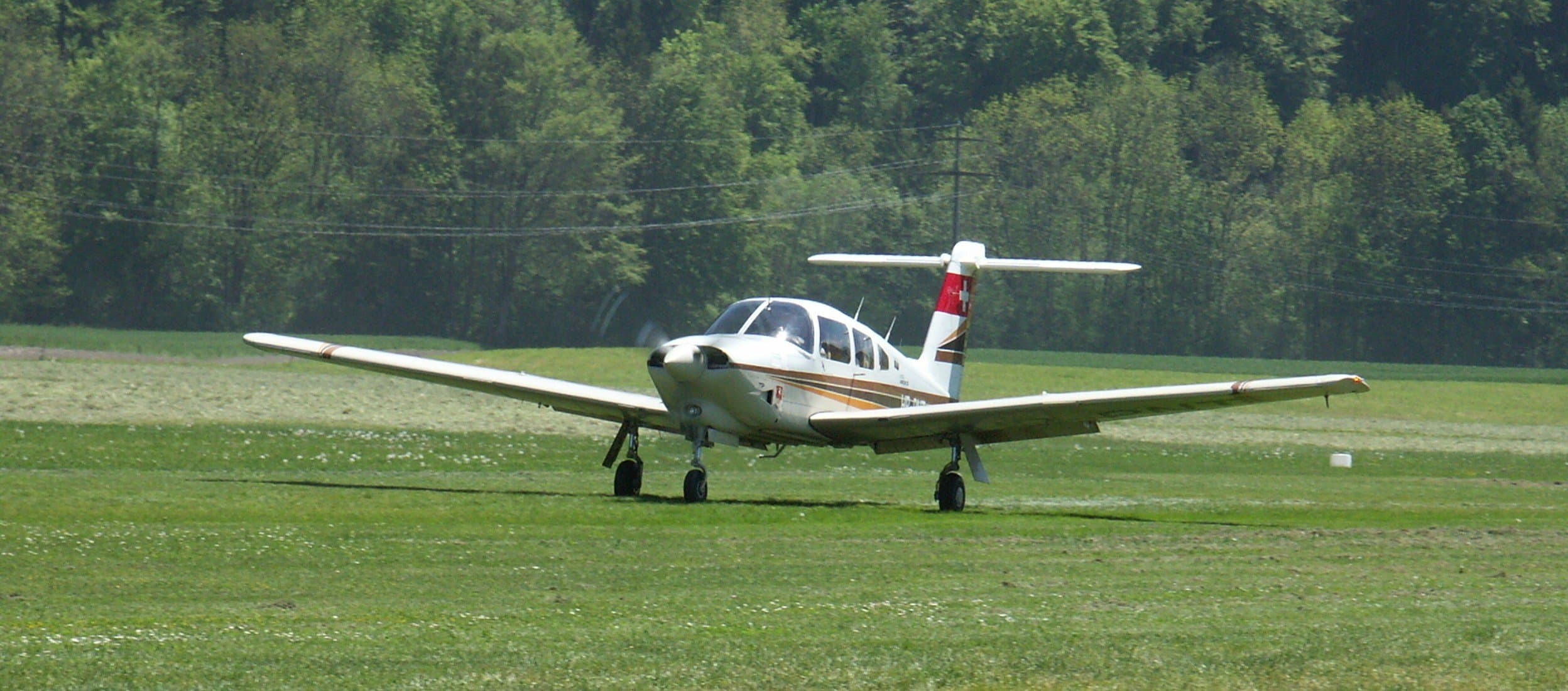 Avion à hélice aux couleurs suisses sur la piste en herbe de la Gruyère