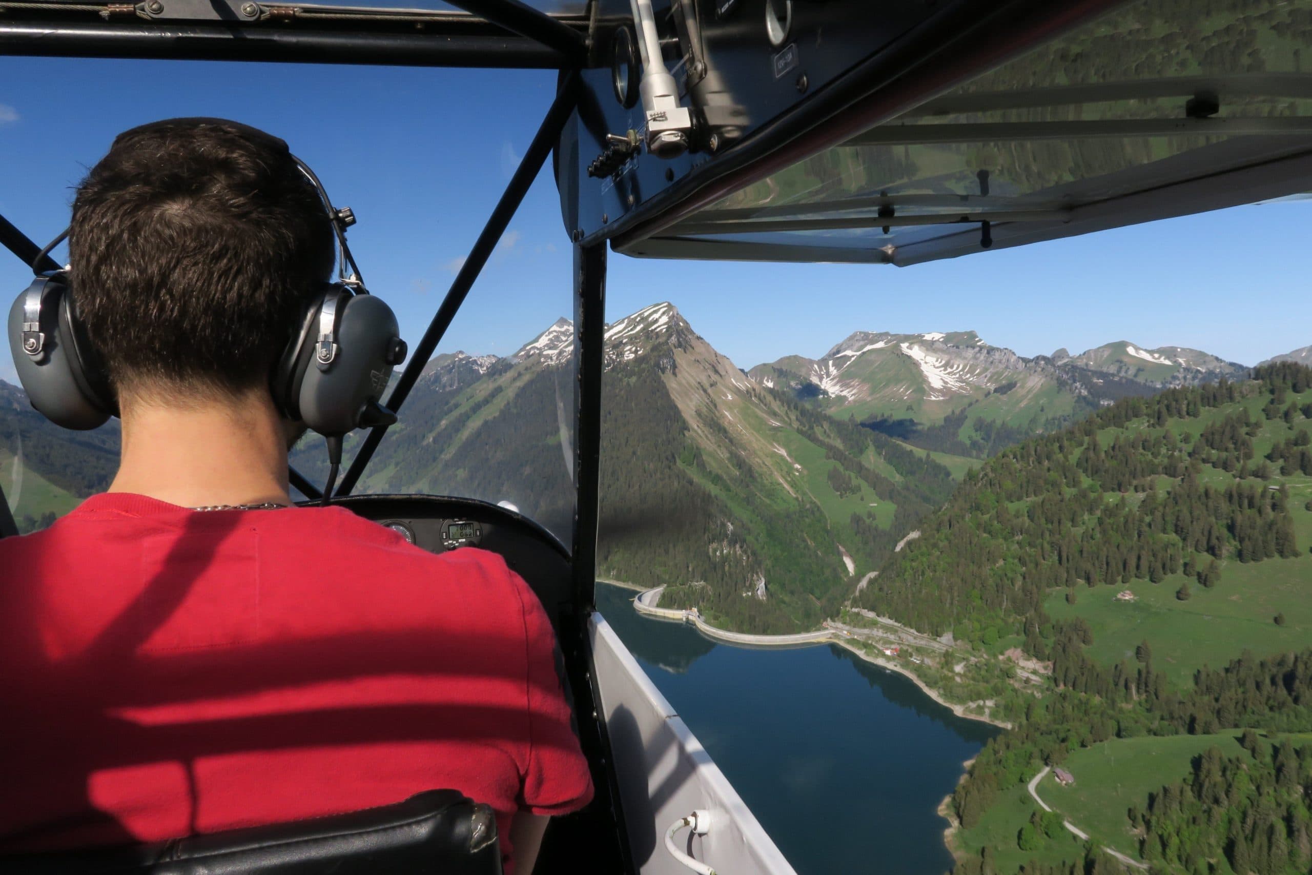 Vue depuis le cockpit d'un avion de l'Aérodrome de la Gruyère survolant un lac de montagne et les Préalpes